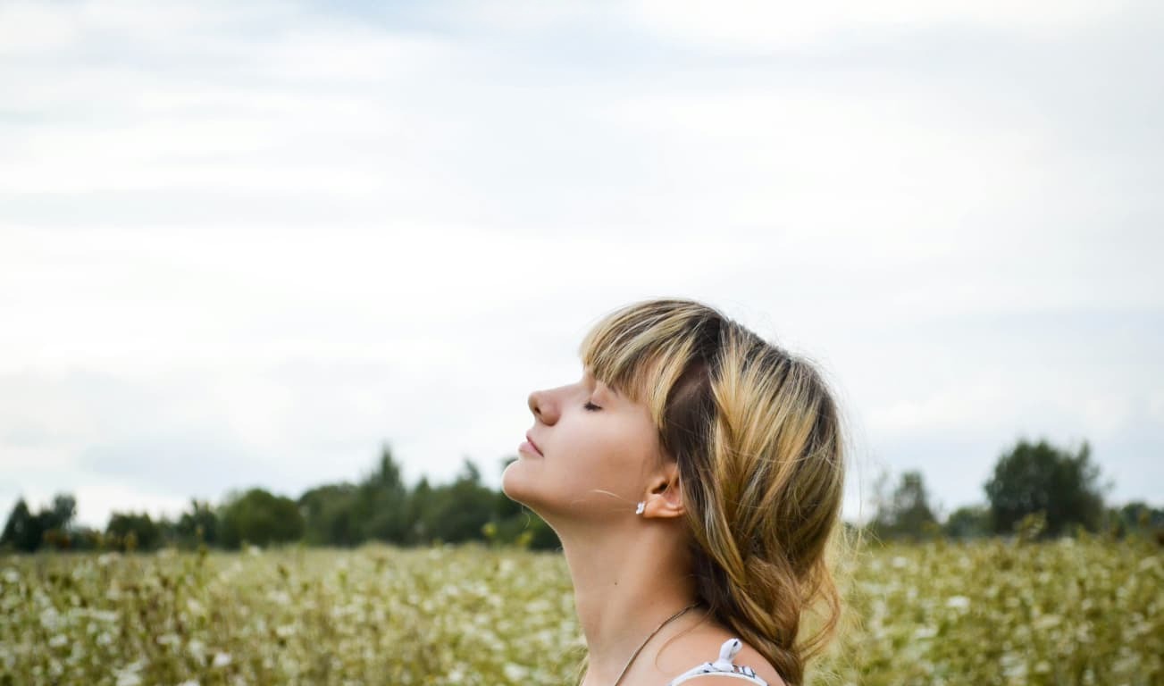 Vrouw met gesloten ogen in een bloeiend veld onder een bewolkte lucht