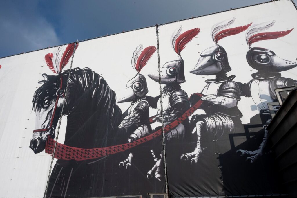 Groot gespannen doek met een zwart-witte tekening van een paard met vier vogelfiguren in harnas en helmen met rode pluimen.